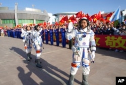 In this photo released by Xinhua News Agency, Chinese astronaut Chen Dong, right, waves as he walks ahead of fellow astronauts Liu Yang and Cai Xuzhe during a sendoff ceremony for the Shenzhou-14 crewed space mission at the Jiuquan Satellite Launch Center