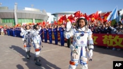 In this photo released by Xinhua News Agency, Chinese astronaut Chen Dong, right, waves as he walks ahead of fellow astronauts Liu Yang and Cai Xuzhe during a sendoff ceremony for the Shenzhou-14 crewed space mission at the Jiuquan Satellite Launch Center