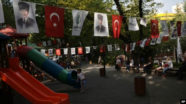 People sit at Kugulu public garden decorated with national flags and images of Turkey's founder Mustafa Kemal Ataturk, in Ankara, Turkey June 2, 2022. (AP Photo/Burhan Ozbilici)