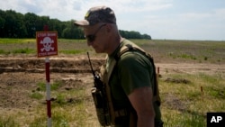 A Ukrainian soldier walks near a post warning about landmines in a field on the outskirts of Kyiv, June 9, 2022.