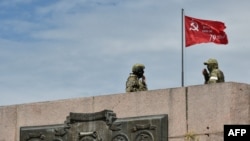 Dua anggota pasukan Rusia tampak berjaga di area yang telah dipasang bendera Uni Soviet yang telah dimodifikasi di Kherson, Ukraina, pada 20 Mei 2022. (Foto: AFP/Olga Maltseva)