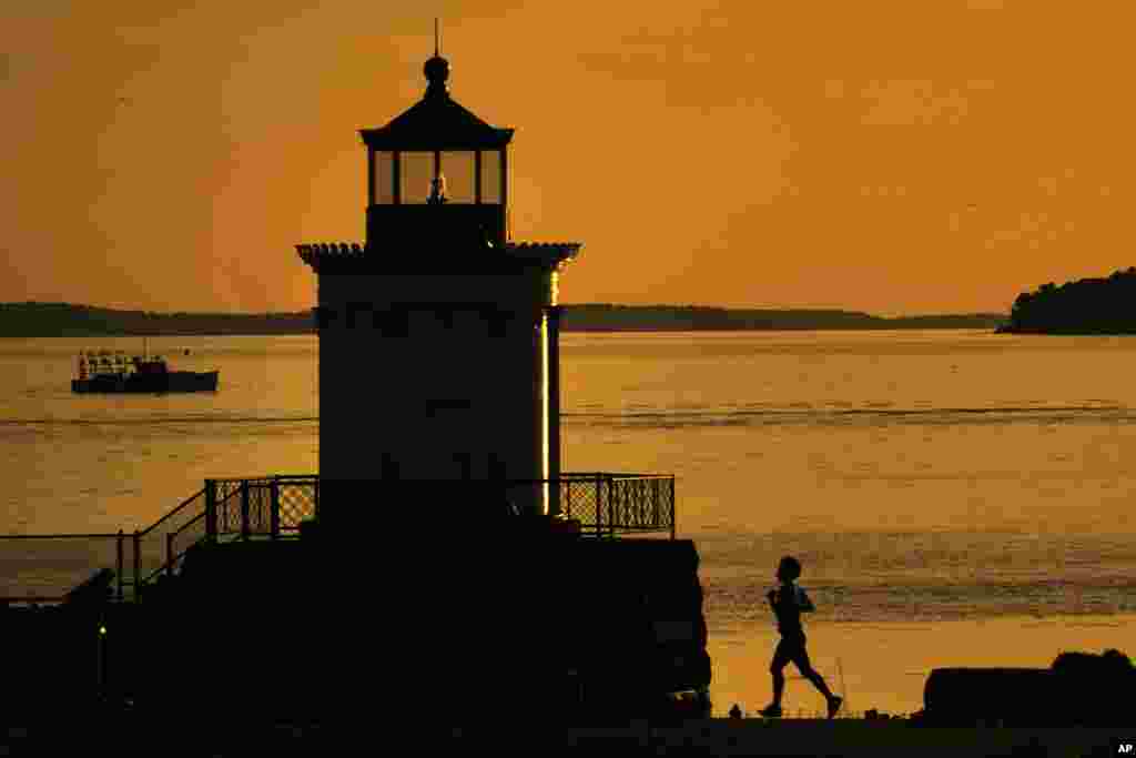 A jogger runs toward Bug Light while a lobster boat heads out of Portland Harbor under calm conditions in South Portland, Maine.