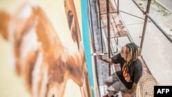 L'artiste brésilien Dos Santos Edgar Bernado, alias Ed-mun, peint au pinceau sur un mur lors du festival Effet Graff, dont l'objectif est de réaliser l'une des plus longues fresques murales du monde, à Cotonou, au Benin, le 18 mai 2022. (Photo YANICK FOL