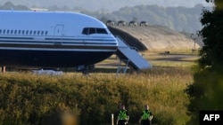 FILE: Two police officers walk near a Boeing 767 sitting on a runway at a military base in Amesbury, Salisbury, on June 14, 2022, preparing to take asylum-seekers to Rwanda. After a last-minute intervention by the European Court of Human Rights, Britain cancele