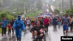 Seorang migran di kursi roda memegang bola saat ia didorong oleh sesama migran, bergabung bersama karavan mereka bertolak dari Tapachula, Meksiko menuju perbatasan AS, 6 Juni 2022. (REUTERS/Quetzalli Nicte-Ha)