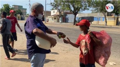 El activista social Oswaldo Díaz reparte mangos a niños, jóvenes y adultos que caminan por una avenida del sector Altos de Milagro Norte, en Maracaibo, Venezuela. [Foto: Gustavo Ocando, VOA]