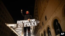 FILE - A protester holds a sign calling for the defunding of police at a protest on July 25, 2020, in Oakland, Calif.