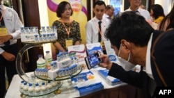 A man uses a mobile phone to take photos of vials of an African swine fever vaccine for pigs displayed during a presentation of the vaccine in Hanoi on June 3, 2022. (Photo by Nhac NGUYEN / AFP)