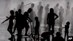 Children and adults cool off in a fountain in a park by the river in Madrid, Spain, June 12, 2022. 