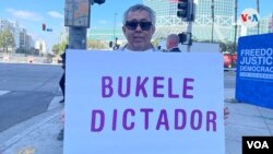 El salvadoreño Mauricio Chávez, que lleva cuatro décadas viviendo en EEUU, posa frente al Centro de Convenciones de Los Ángeles con un cartel que dice “Bukele Dictador”. [Foto: VOA / Antoni Belchi]