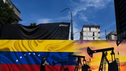 Un hombre con cubrebocas pasa junto a un mural que representa una bomba de aceite y la bandera venezolana en una calle de Caracas, el 26 de mayo de 2022.