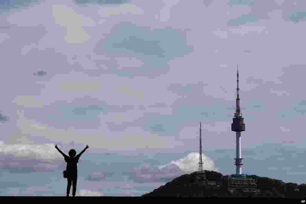 A woman stands for a photo as she is seen against the sky and the N Seoul Tower at the National Museum of Korea in Seoul, South Korea.