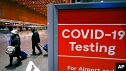 FILE - Travelers pass a sign near a COVID-19 testing site in Terminal E at Logan Airport, in Boston, Dec. 21, 2021.