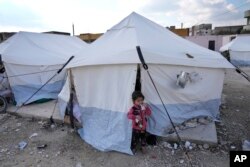 Seorang gadis yang keluarganya kehilangan rumahnya akibat gempa dahsyat, berdiri di luar tenda di kamp penampungan di Killi, Suriah, Minggu, 12 Februari 2023. (AP/Hussein Malla)