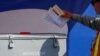 FILE -: An election worker places mail-in ballots into an election box at a drive-through drop off location at the Registrar of Voters in San Diego, California.