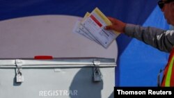 FILE -: An election worker places mail-in ballots into an election box at a drive-through drop off location at the Registrar of Voters in San Diego, California.