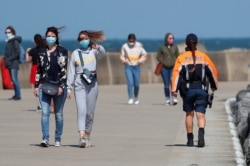 Tourists wearing protective face masks walk along the North Sea breakwater next to a police officer as Belgian coastal towns impose masks on dykes in Ostend, Belgium, July 28, 2020.