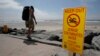 FILE - A beachgoer walks past a sign posted to warn people of contaminated water at Torrey Pines State Beach in San Diego, California.