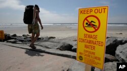 FILE - A beachgoer walks past a sign posted to warn people of contaminated water at Torrey Pines State Beach in San Diego, California.