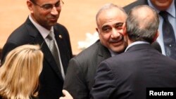 Iraq's new Oil Minister Adel Abdul-Mehdi, front facing, greets Iranian Ambassador to Iraq Hassan Danaifar, right, during a parliamentary session to vote on Iraq's new government at the parliament headquarters in Baghdad, Sept. 8, 2014. 