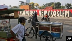 Penjaja makanan melewati mural di tengah wabah virus corona di Jakarta, Senin, 8 Juni 2020. (Foto: AP)