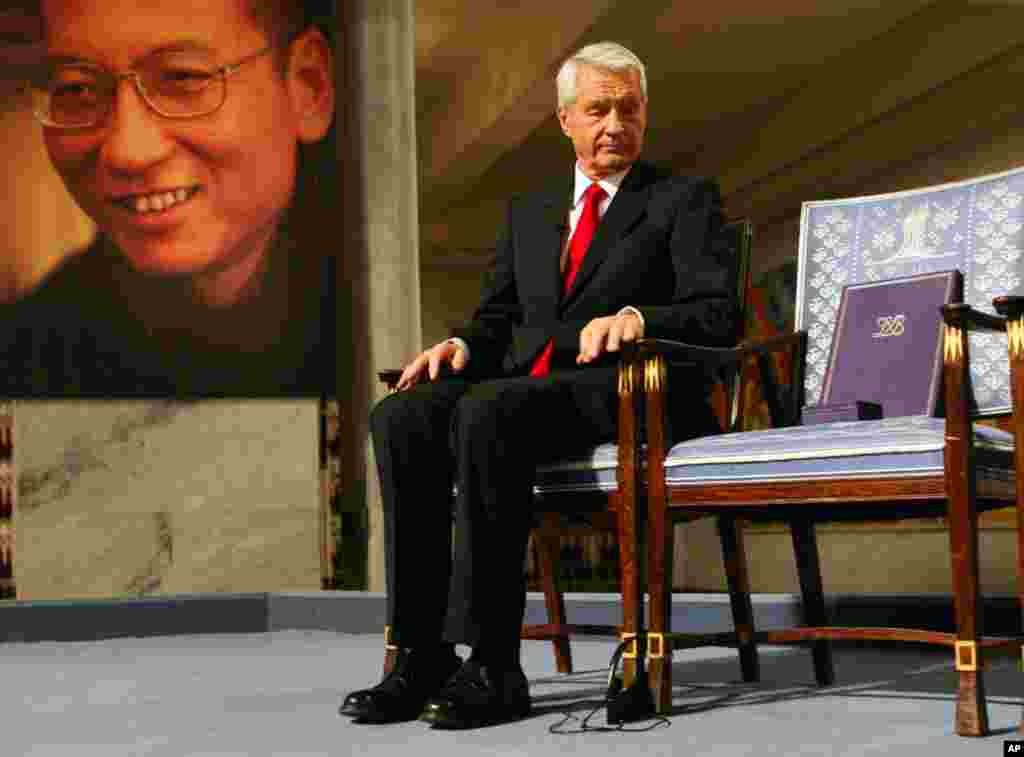 Chairman of the Norwegian Nobel Committee Thorbjoern Jagland looks down at the Nobel certificate and medal on the empty chair where this year's Nobel Peace Prize winner jailed Chinese dissident Liu Xiaobo would have sat, as a portrait of Liu is seen in th