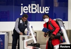 Seorang karyawan JetBlue Airlines (tanpa masker) membantu check-in barang bawaan penumpang (mengenakan masker) di Bandara Nasional Ronald Reagan Washington di Arlington, Virginia, 19 April 2022. (REUTERS/Kevin Lamarque)