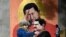 Một người đi ngang qua tranh tường vẽ cố TT Hugo Chavez, giữa, giơ tay chào TT Nicolas Maduro, phải, đang bồng một đừa trẻ ở Caracas. (Photo by Federico PARRA / AFP)