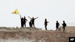 Fighters with the Kurdish People's Protection Units, or YPG, wave their yellow triangular flag on the outskirts of Tal Abyad, Syria, June 15, 2015.