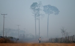FILE - A man walks amid smoke from a burning tract of Amazon jungle as it is cleared by loggers and farmers near Porto Velho, Brazil, Aug. 28, 2019.