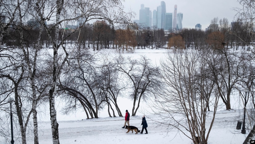Orang-orang berjalan-jalan dengan anjing mereka di tengah salju, dengan latar belakang gedung pencakar langit Kota Moskow, di Moskow, Rusia, Rabu, 5 Februari 2020. (Foto: AP/Pavel Golovkin)