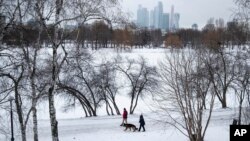 Orang-orang berjalan-jalan dengan anjing mereka di tengah salju, dengan latar belakang gedung pencakar langit Kota Moskow, di Moskow, Rusia, Rabu, 5 Februari 2020. (Foto: AP/Pavel Golovkin)