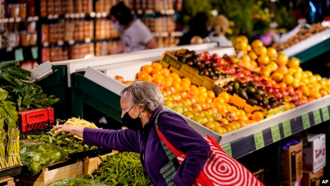 FILE - A shopper wearing a protective mask as a precaution against the spread of the coronavirus selects produce at the Reading Terminal Market in Philadelphia, Friday, April 22, 2022. (AP Photo/Matt Rourke)