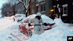 Una mujer palea la nieve cubre su auto y la entrada a la casa en Albany, Nueva York.