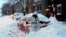 Una mujer palea la nieve cubre su auto y la entrada a la casa en Albany, Nueva York.