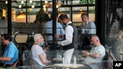 A waiter wearing a face mask serves at a restaurant terrace in Paris, July 26, 2021, as France's parliament approved a law requiring special virus passes for all restaurants and domestic travel, and mandating vaccinations for all health workers.