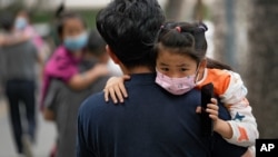 People carrying children wearing face masks to help curb the spread of the coronavirus head to a kindergarten in Beijing on June 9, 2021.