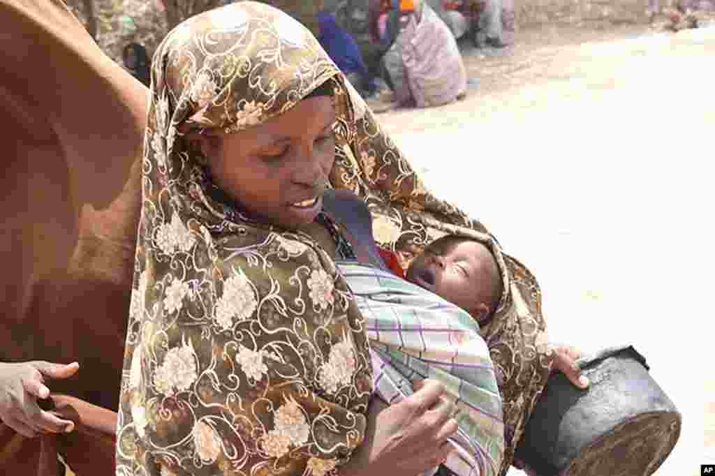 Woman carrying baby asleep going to get food at Badbaado IDP camp in Mogadishu, Somalia, August 11, 2011. (VOA - P. Heinlein)