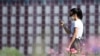 FILE - A young woman wearing a face mask to protect against the coronavirus checks her phone in a park in the Porta Nuova district, in Milan, Italy, May 4, 2020.