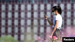 FILE - A young woman wearing a face mask to protect against the coronavirus checks her phone in a park in the Porta Nuova district, in Milan, Italy, May 4, 2020.