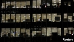 FILE - Workers are seen in office windows in the financial district of Canary Wharf in London, Nov. 3, 2015. 