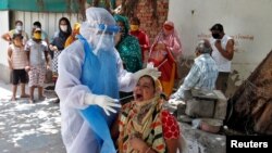 A woman reacts as a healthcare worker wearing a protective gear takes a swab to test for the coronavirus disease (COVID-19) at a residential area in Ahmedabad, India that saw its biggest single-day spike since the pandemic began, May 22, 2020.