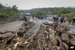 FILE — Passengers from stranded vehicles stand next to the debris from floodwaters, on the road from Kapenguria, in West Pokot county, in western Kenya Saturday, Nov. 23, 2019.