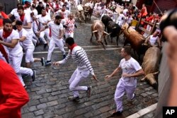 Orang-orang berlarian di jalan pada hari pertama adu banteng dan sapi, dalam perayaan San Fermín di Pamplona, Spanyol utara, Selasa, 7 Juli 2022. (AP/Álvaro Barrientos)