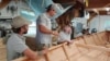 Apprentice program instructors Chris Cease, left, and Gabe Beckerman provide tips on building a sailboat to two of the apprentices. (Deborah Block/VOA)