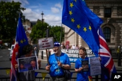 Protesters, one of them holding a photograph of British Prime Minister Boris Johnson and Britain's Home Secretary Priti Patel, stand outside the Houses of Parliament, in London, July 6, 2022.