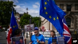 FILE - Protesters, one holding a photo of British Prime Minister Boris Johnson and Britain's Home Secretary Priti Patel, outside the Houses of Parliament, in London, July 6, 2022.