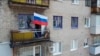 In this handout photo taken from video and released by Russian Defense Ministry Press Service July 4, 2022, a man sets a Russian national flag on a balcony of a residential building in Lysychansk, Luhansk province, eastern Ukraine.