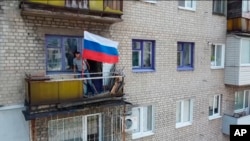 FILE - In this handout photo taken from video and released by Russian Defense Ministry Press Service July 4, 2022, a man sets a Russian national flag on a balcony of a residential building in Lysychansk, Luhansk province, eastern Ukraine.