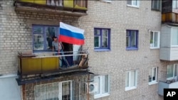 In this handout photo taken from video and released by Russian Defense Ministry Press Service July 4, 2022, a man sets a Russian national flag on a balcony of a residential building in Lysychansk, Luhansk province, eastern Ukraine.